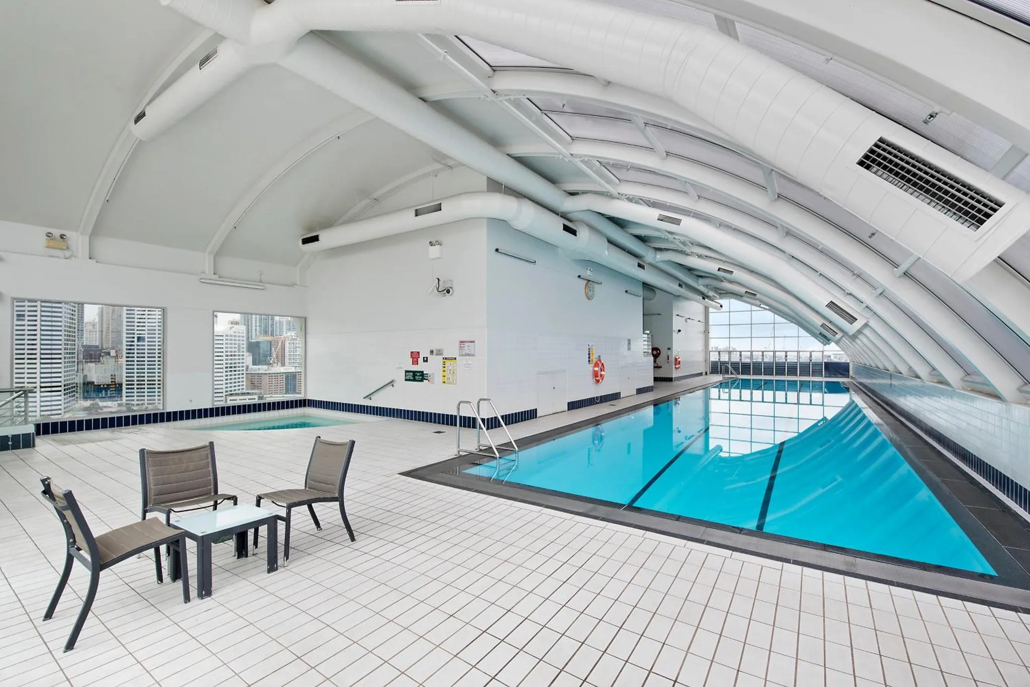 Une piscine intérieure lumineuse avec des chaises longues et une vue sur la ville.