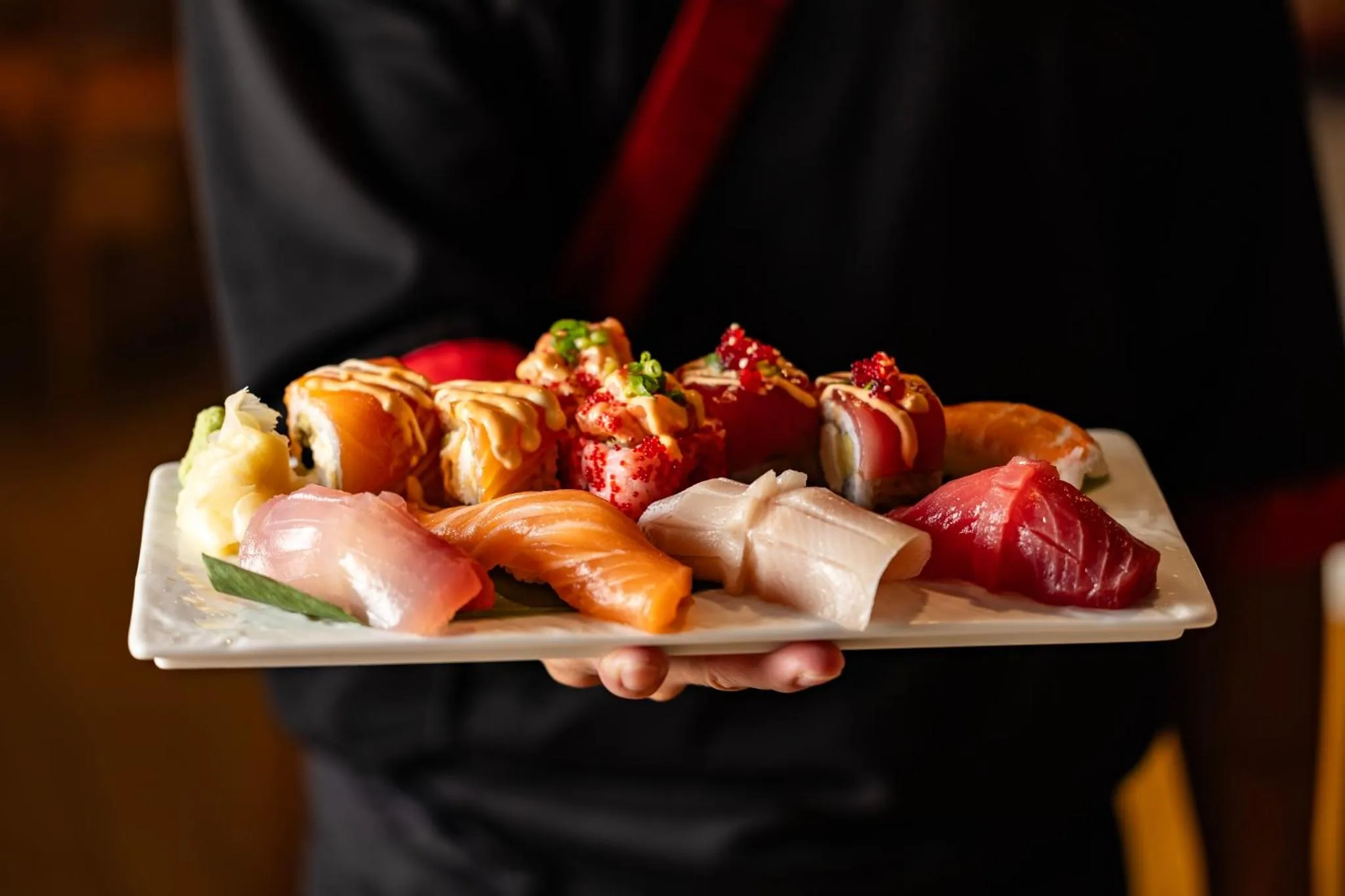 Assiette de sushis et de sashimis présentée par une personne.