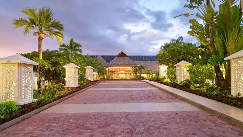 Allée pavée menant à l'entrée illuminée d'un bâtiment tropical.