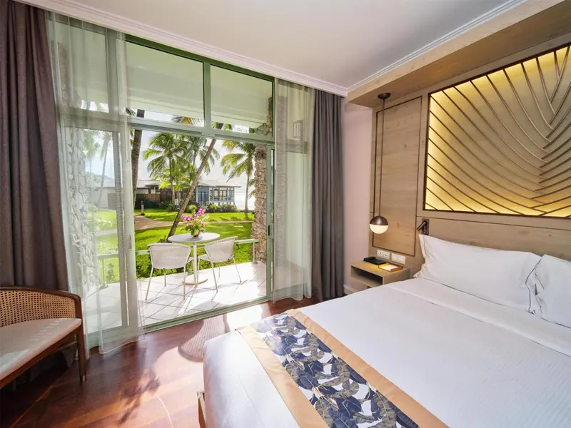 Une chambre lumineuse s'ouvre sur une terrasse avec vue sur un jardin tropical.