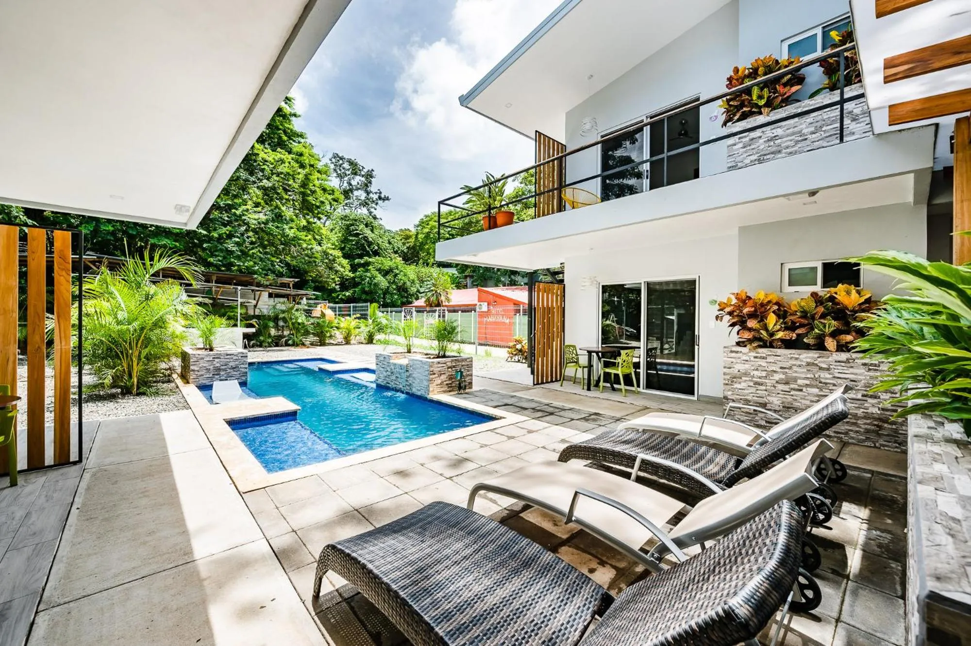 Transats et piscine devant un bâtiment moderne avec végétation luxuriante.