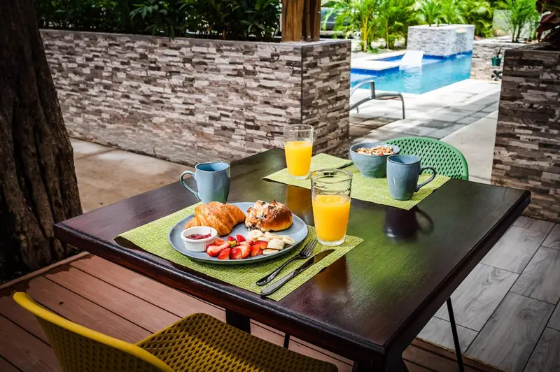 Une table est dressée avec un petit-déjeuner composé de viennoiseries, de fruits et de boissons.