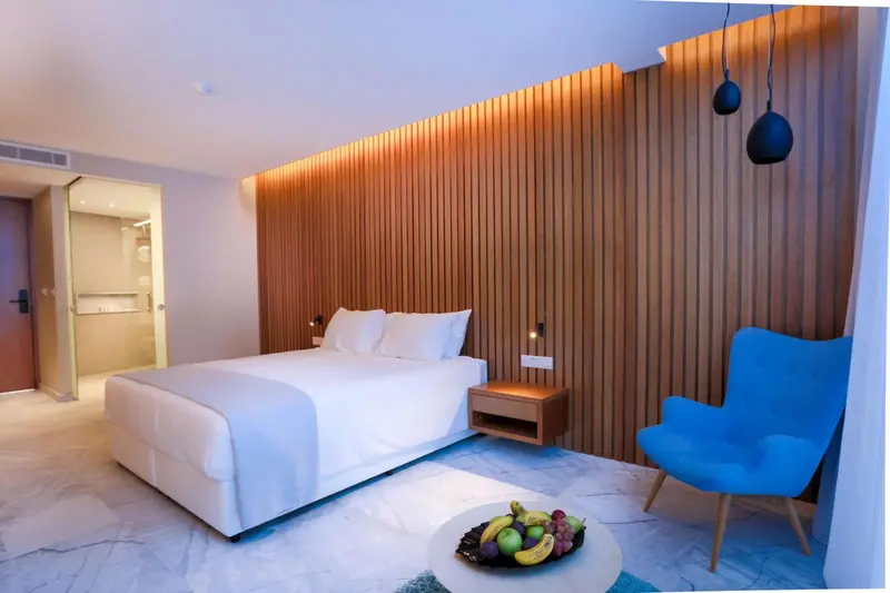 Une chambre lumineuse avec un lit blanc et un fauteuil bleu.