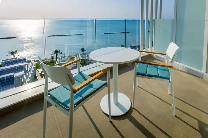 Une table ronde et deux chaises blanches sur une terrasse ensoleillée avec vue sur la mer.