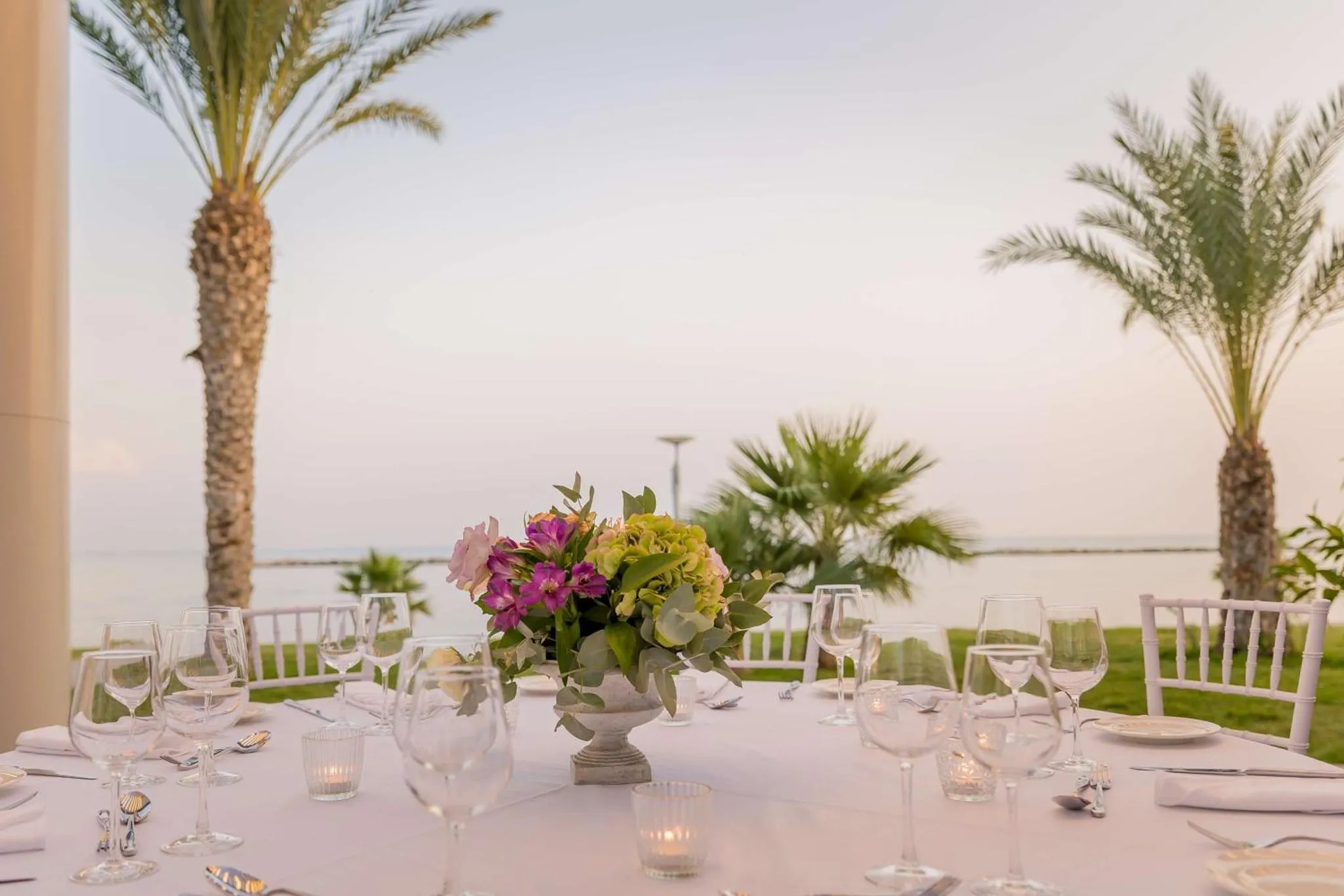 Une table dressée avec des verres et des fleurs devant une vue sur la mer.