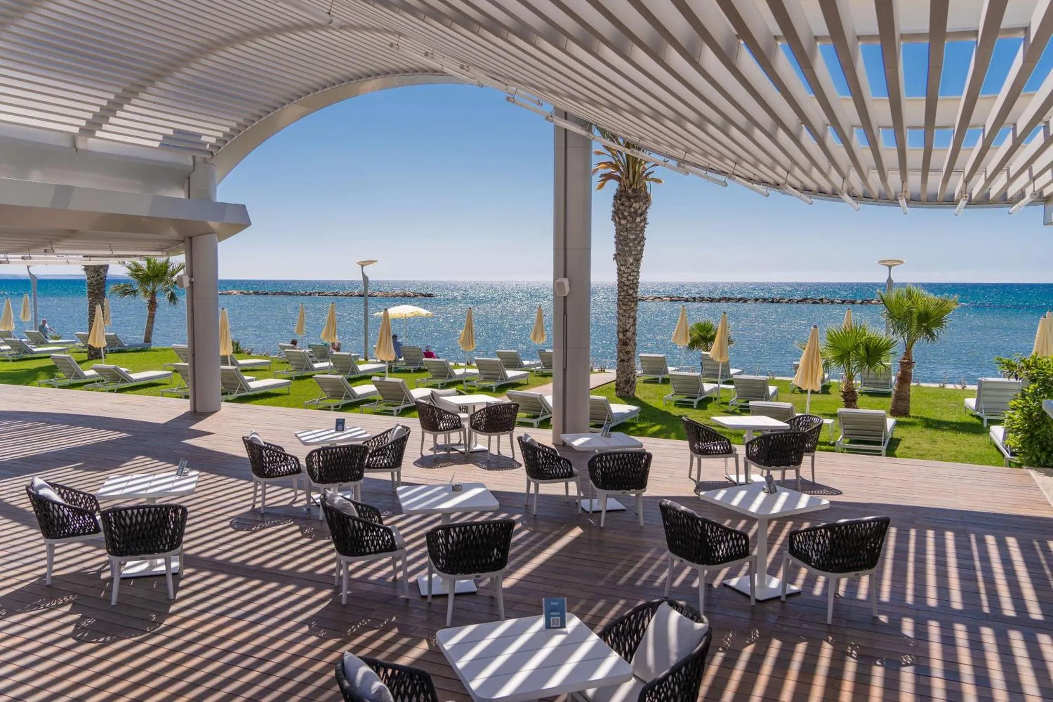 Terrasse ombragée avec tables et chaises donnant sur la mer.