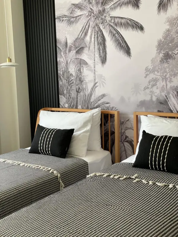 Deux lits simples avec oreillers et couvertures dans une chambre décorée d'un grand motif de palmiers.