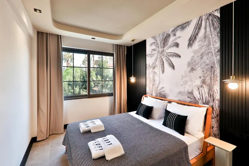 Une chambre lumineuse avec un grand lit et un mur décoré de palmiers.