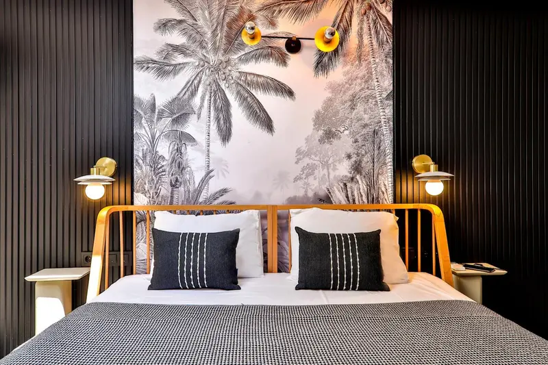 Lit double avec oreillers et couvertures blanches dans une chambre décorée de motifs tropicaux.