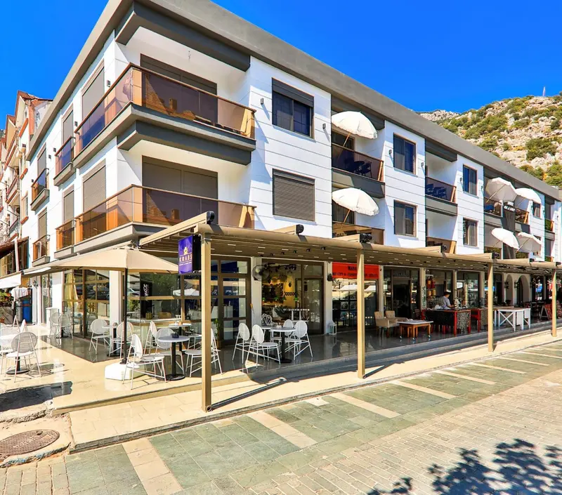 Façade d'un bâtiment blanc avec des terrasses ombragées et des tables de café en contrebas.