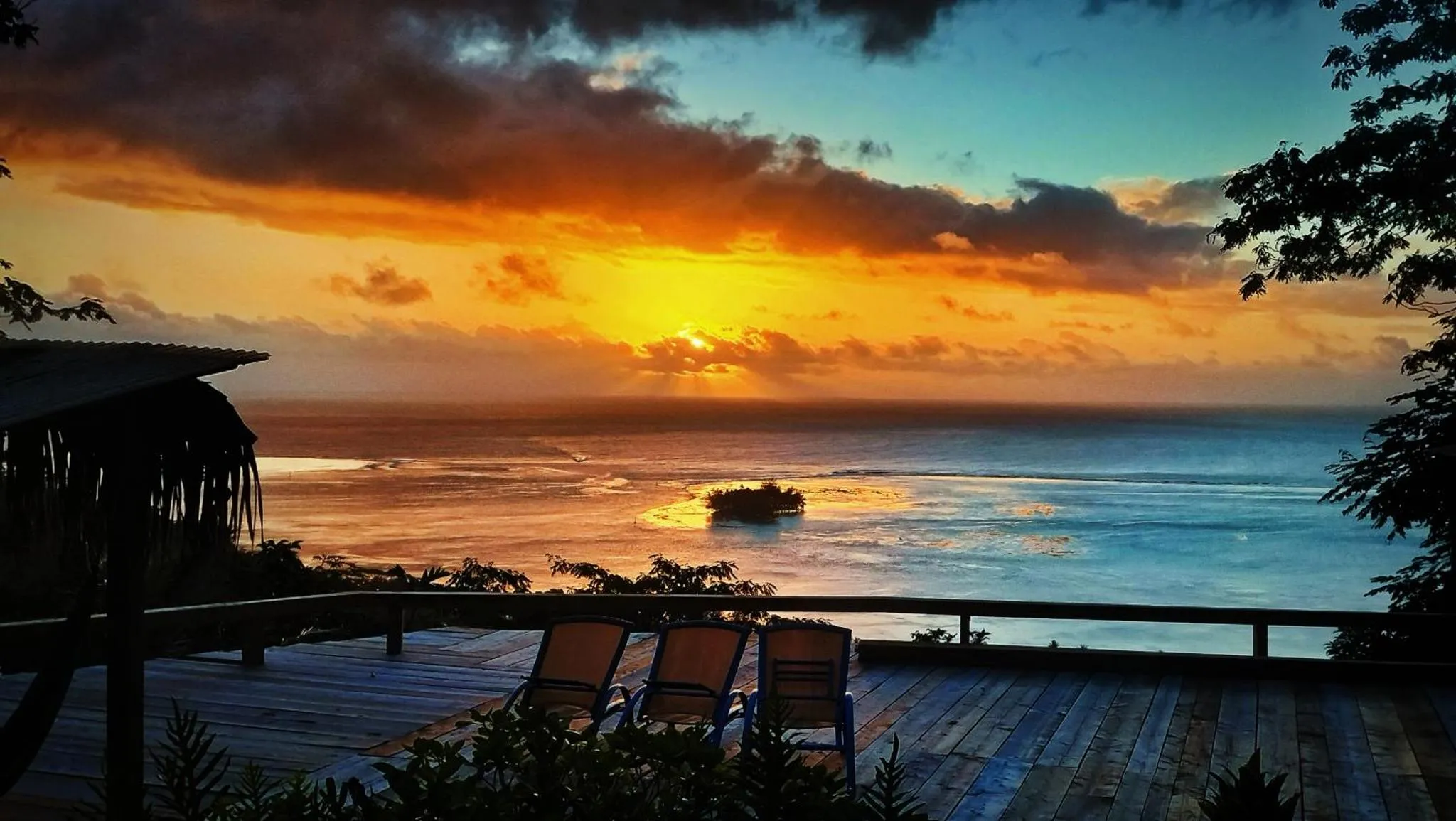 Terrasse en bois avec transats face à la mer au coucher du soleil.