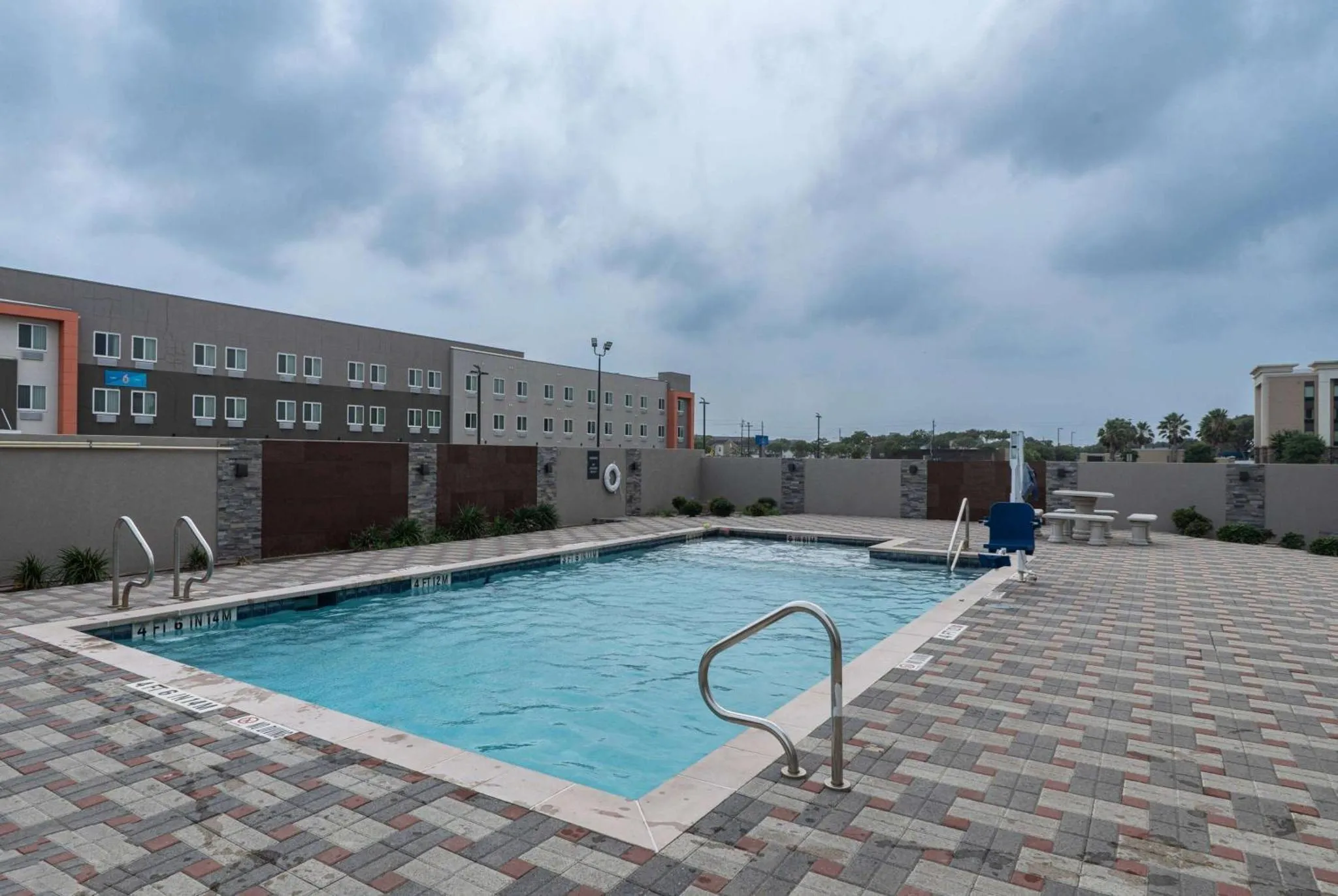 Piscine rectangulaire entourée d'une terrasse pavée devant un bâtiment à étages.