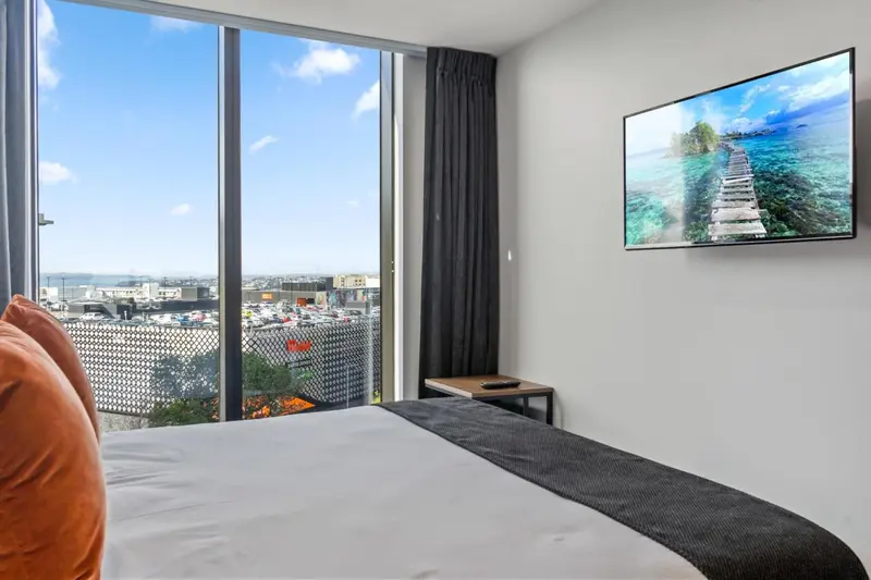Chambre avec un grand lit et une vue sur la ville à travers de larges fenêtres.
