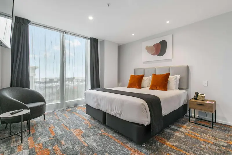 Chambre moderne avec un grand lit et un coin salon près d'une fenêtre.