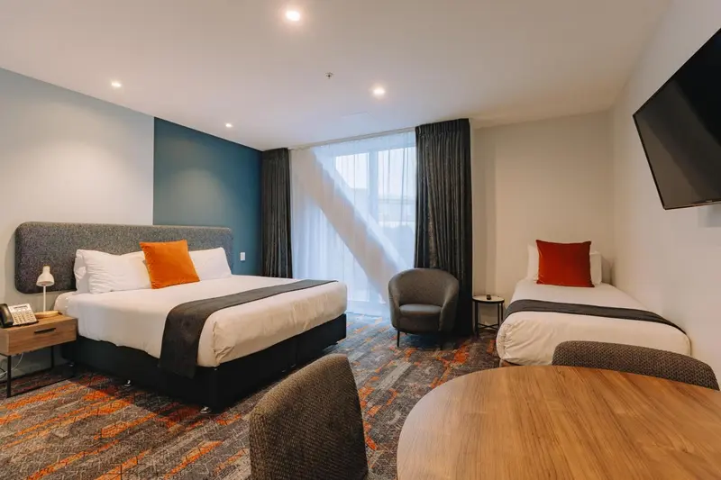 Chambre avec un grand lit et un lit simple, éclairée par une fenêtre.