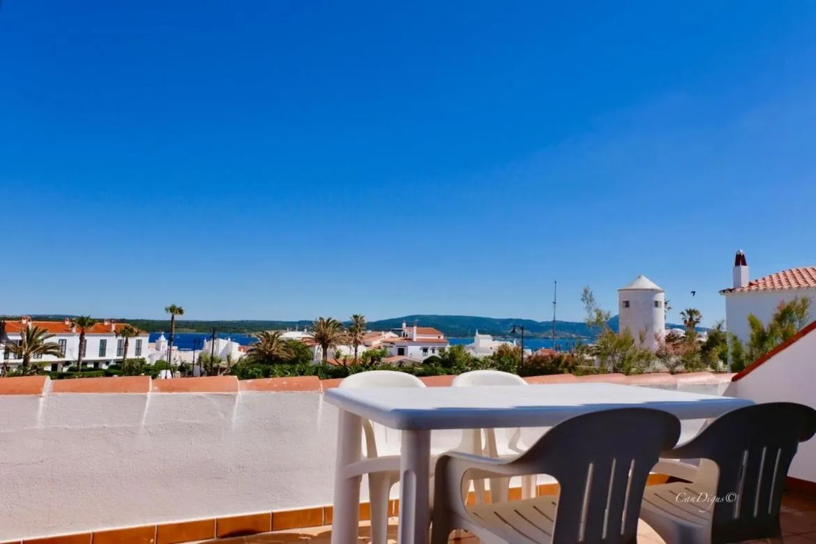 Une table et des chaises en plastique sur une terrasse ensoleillée avec vue sur la mer et un village.