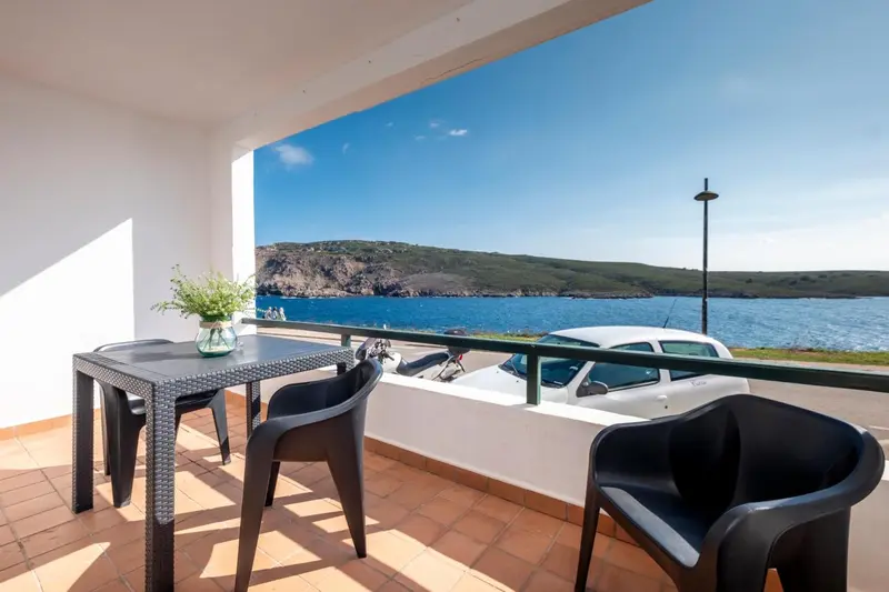 Terrasse avec table et chaises donnant sur la mer et la côte.