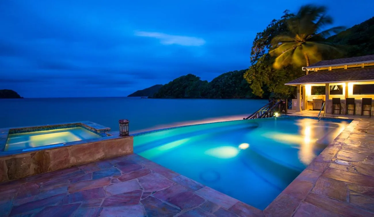 Piscine illuminée avec jacuzzi et vue sur la mer au crépuscule.