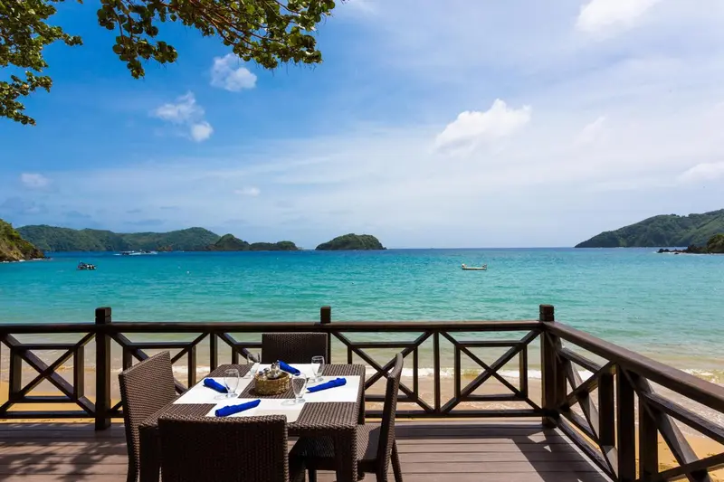 Une table est dressée sur une terrasse en bois face à une baie turquoise.