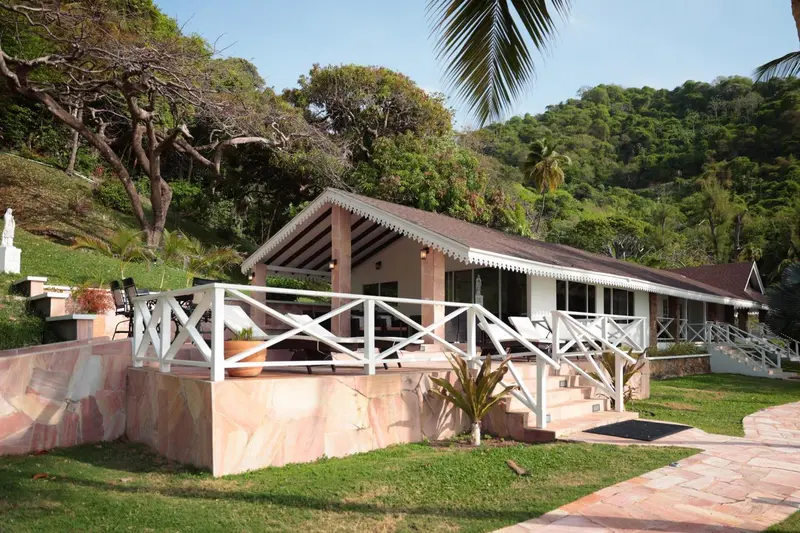Bâtiment blanc avec terrasse et végétation luxuriante en arrière-plan.