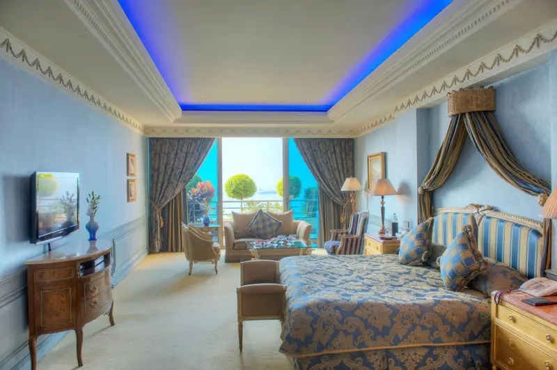 Une chambre lumineuse avec un grand lit et un coin salon donnant sur une vue turquoise.