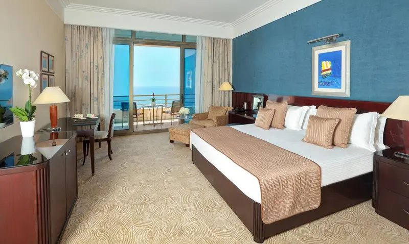 Une chambre lumineuse avec un grand lit et un accès à un balcon avec vue sur la mer.