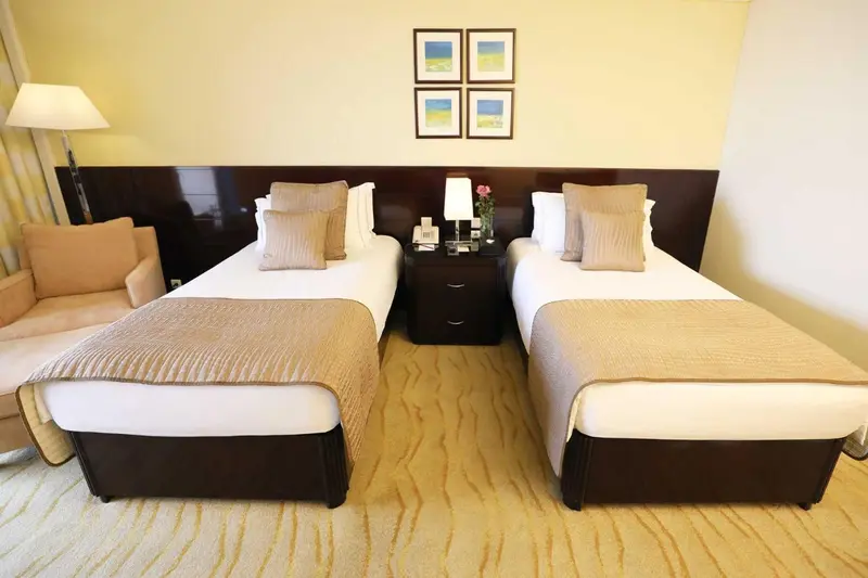 Une chambre lumineuse avec deux lits simples et un canape beige.