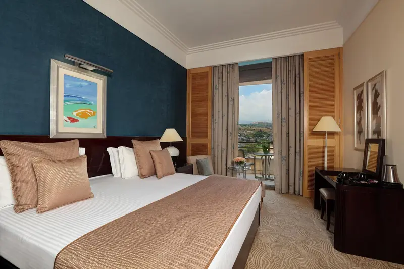 Une chambre lumineuse avec un grand lit et un balcon offrant une vue sur le paysage.