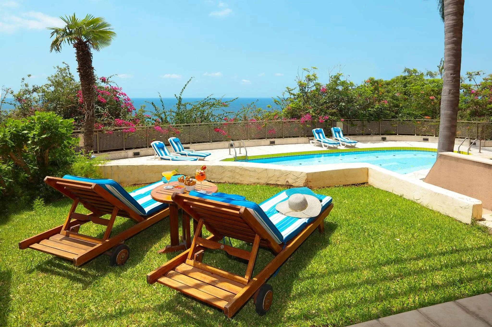 Transats et table basse avec boisson au bord d'une piscine ensoleillée.