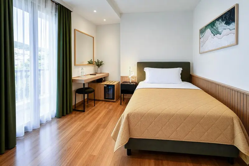 Chambre lumineuse avec un lit simple et un bureau près d'une fenêtre.