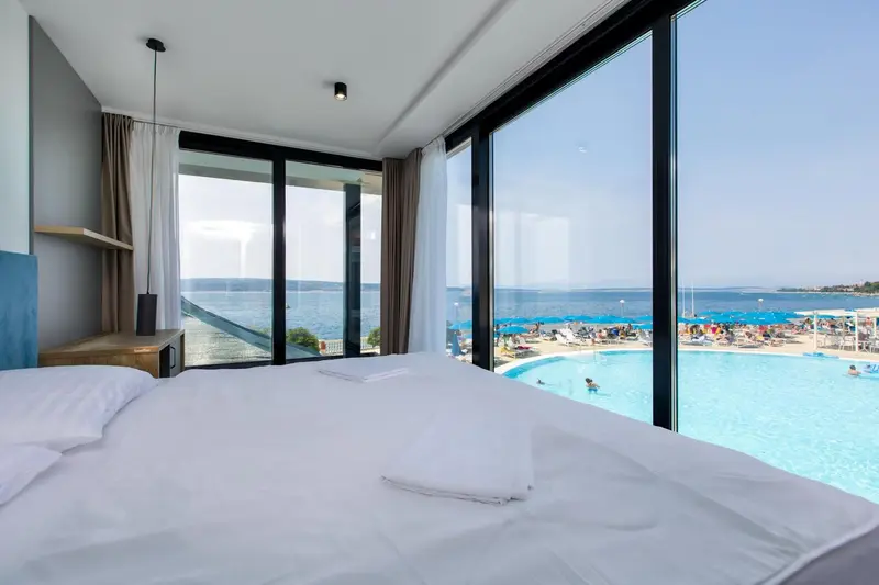 Une chambre lumineuse avec un grand lit donnant sur une piscine et la mer.
