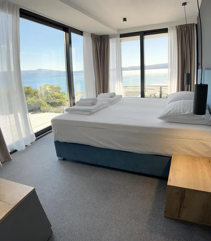 Une chambre lumineuse avec un grand lit face à une baie vitrée donnant sur la mer.