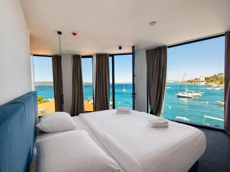 Chambre lumineuse avec un grand lit donnant sur une vue mer et un port de plaisance.