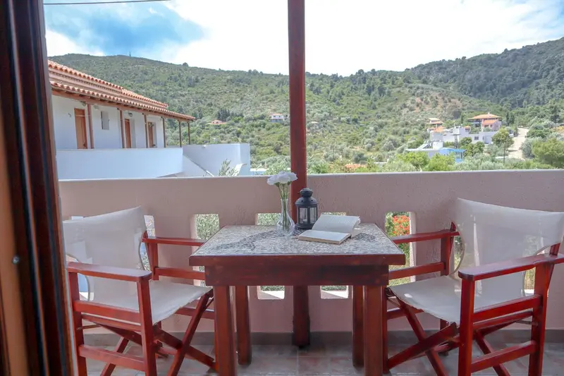 Une table et deux chaises se trouvent sur un balcon avec vue sur les collines.