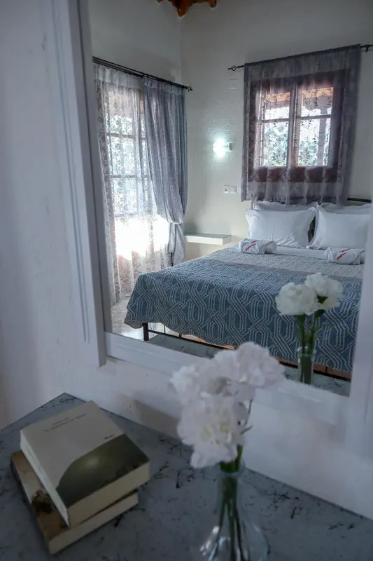 Une chambre lumineuse avec un lit recouvert d'une courtepointe bleue et des fleurs blanches sur une table de chevet.