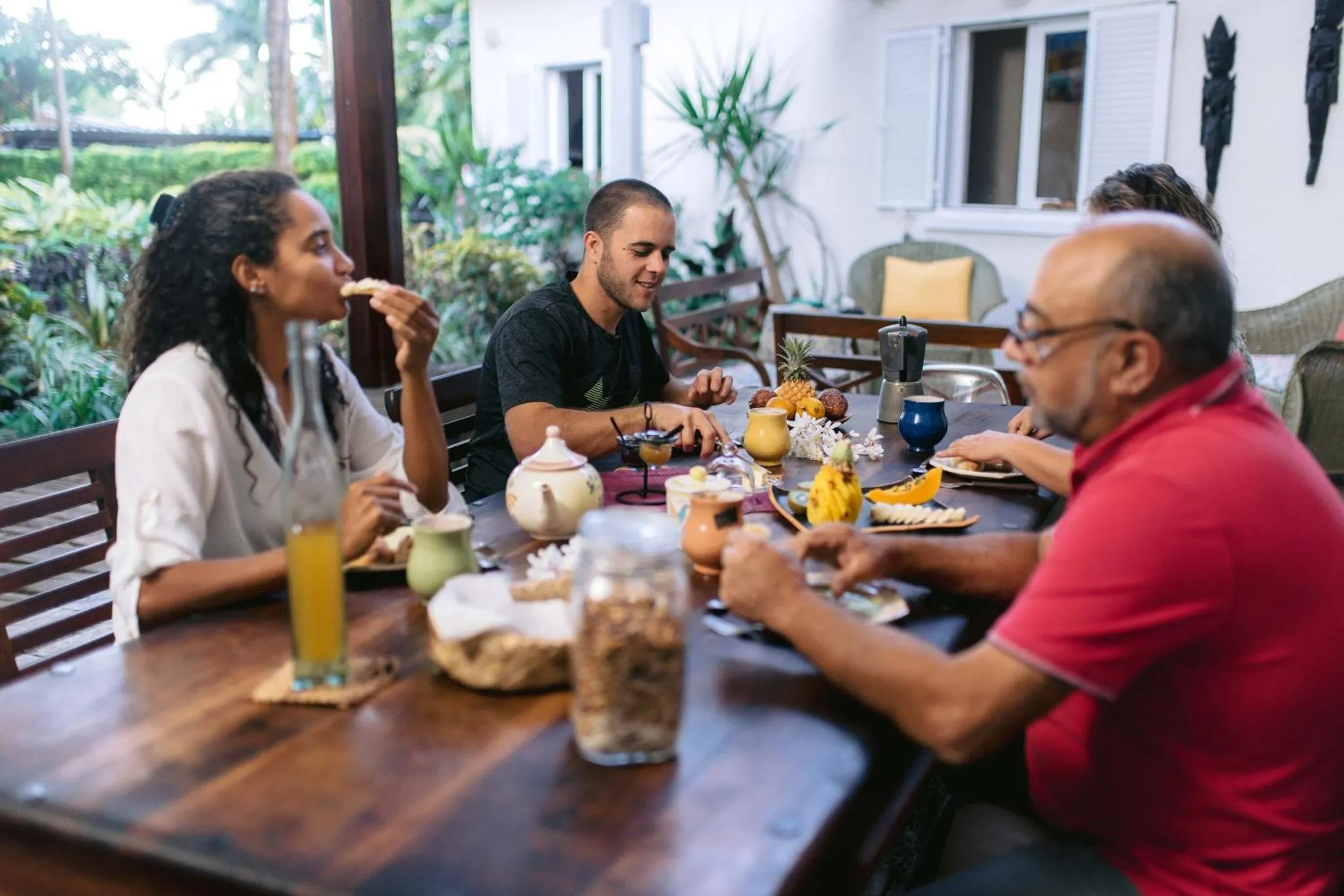Des convives déjeunent à une table en bois sur une terrasse ombragée.