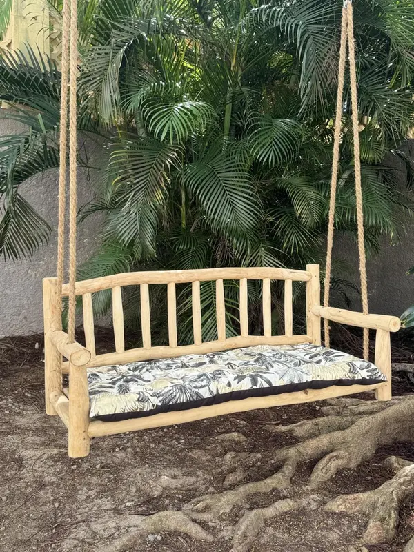 Balançoire en bois rustique avec coussin à motifs végétaux devant une végétation luxuriante.