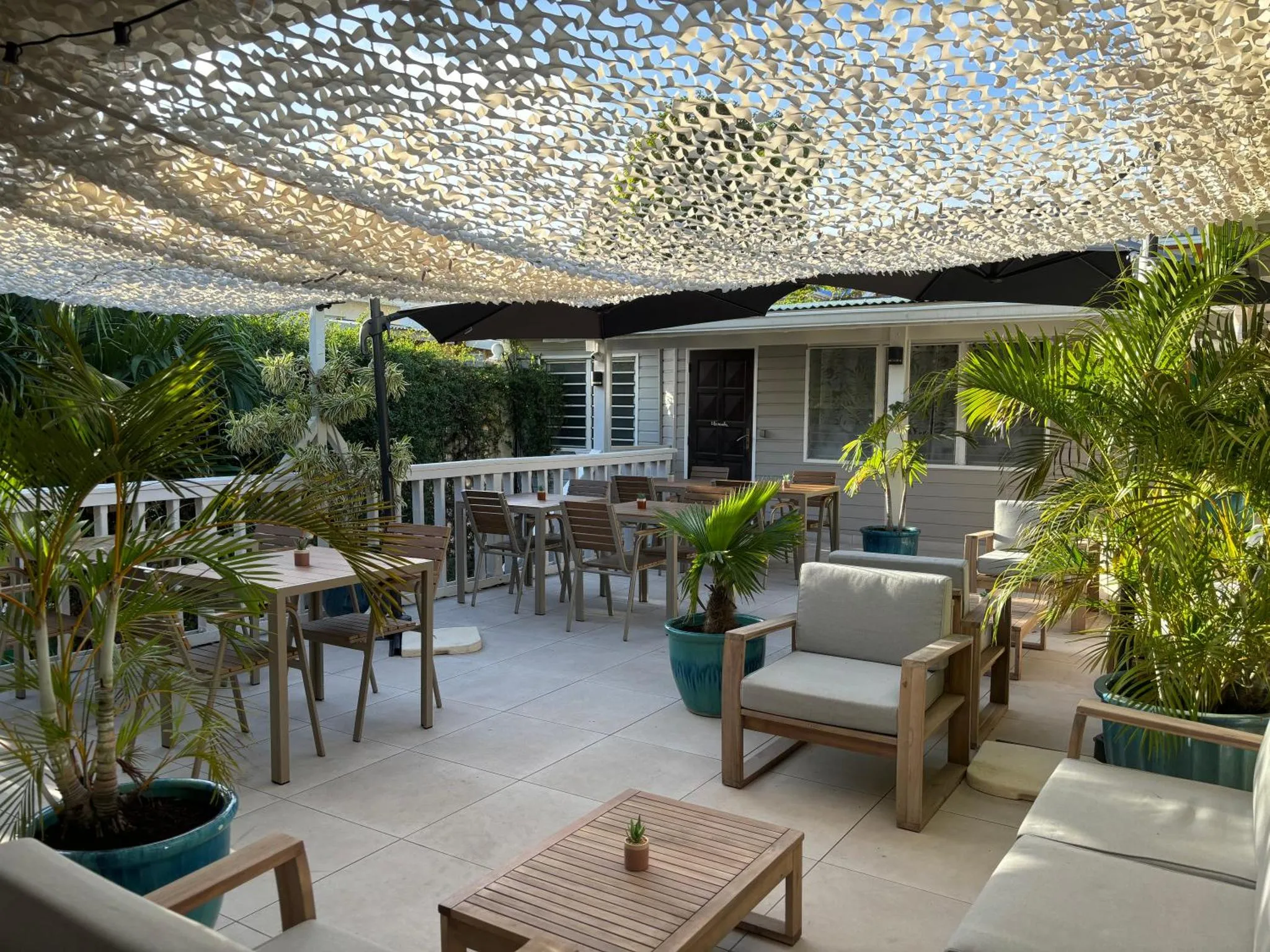 Terrasse ombragée avec tables et canapés en bois.