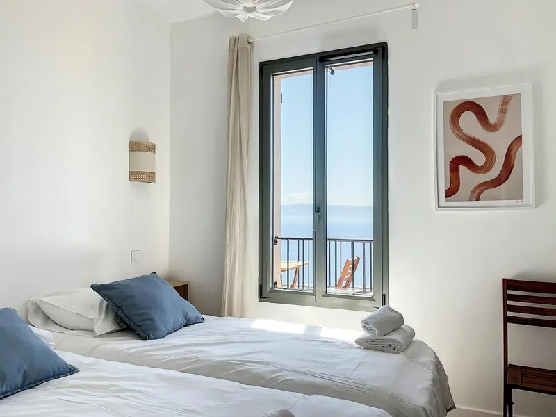 Chambre lumineuse avec vue sur la mer depuis un balcon.