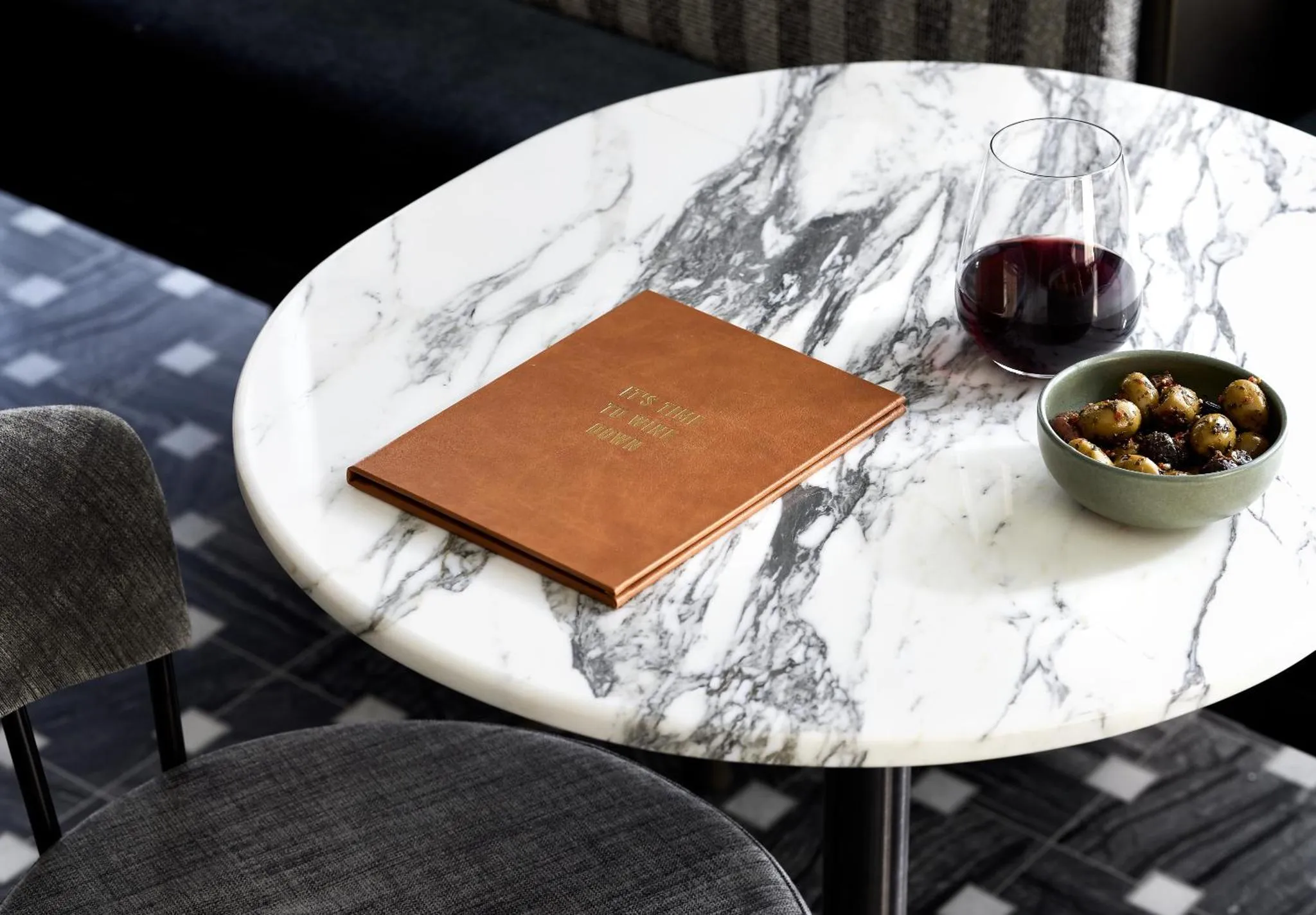 Une table ronde en marbre présente un menu, un verre de vin rouge et une petite portion de nourriture.