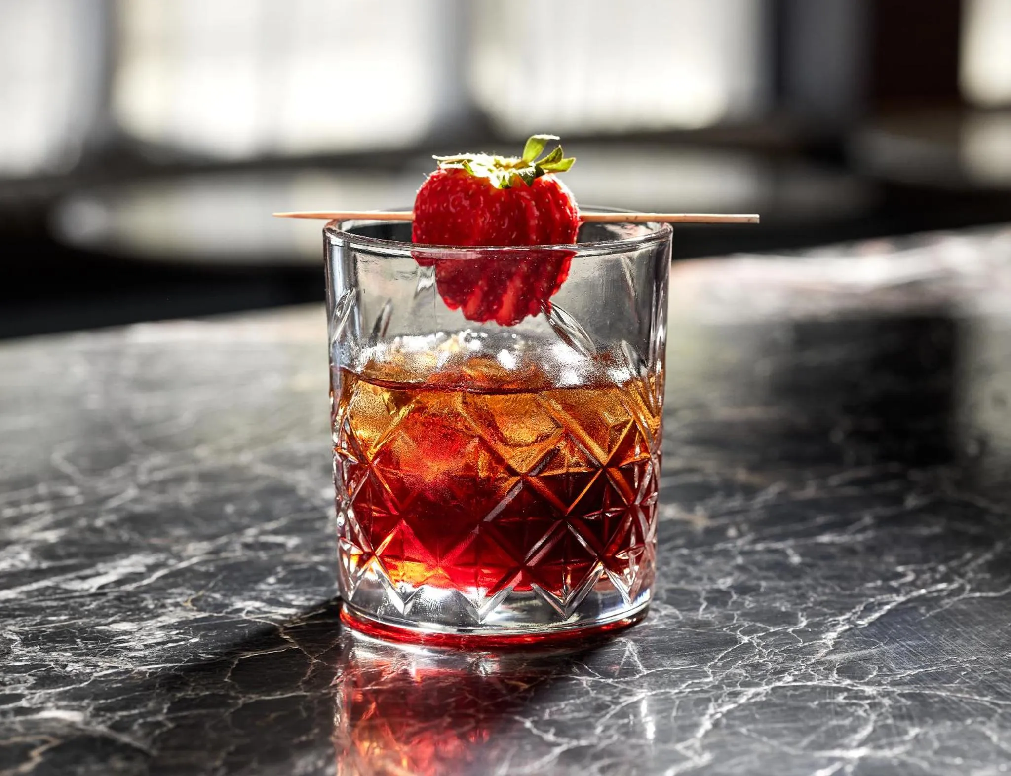 Un verre de cocktail rouge garni d'une fraise est posé sur un comptoir en marbre.