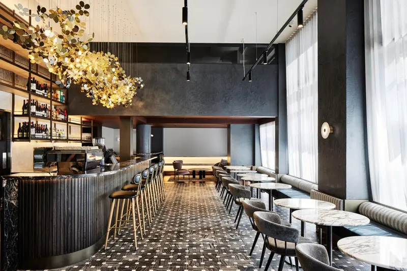 Un long comptoir de bar en marbre noir est aligné avec des tabourets hauts, devant des tables et des banquettes.