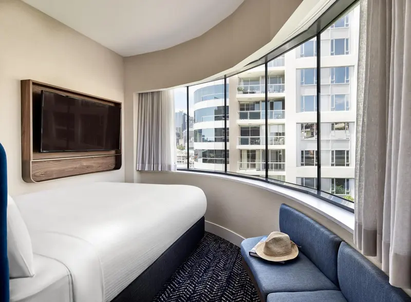 Une chambre lumineuse avec un grand lit et un coin salon près d'une fenêtre cintrée.