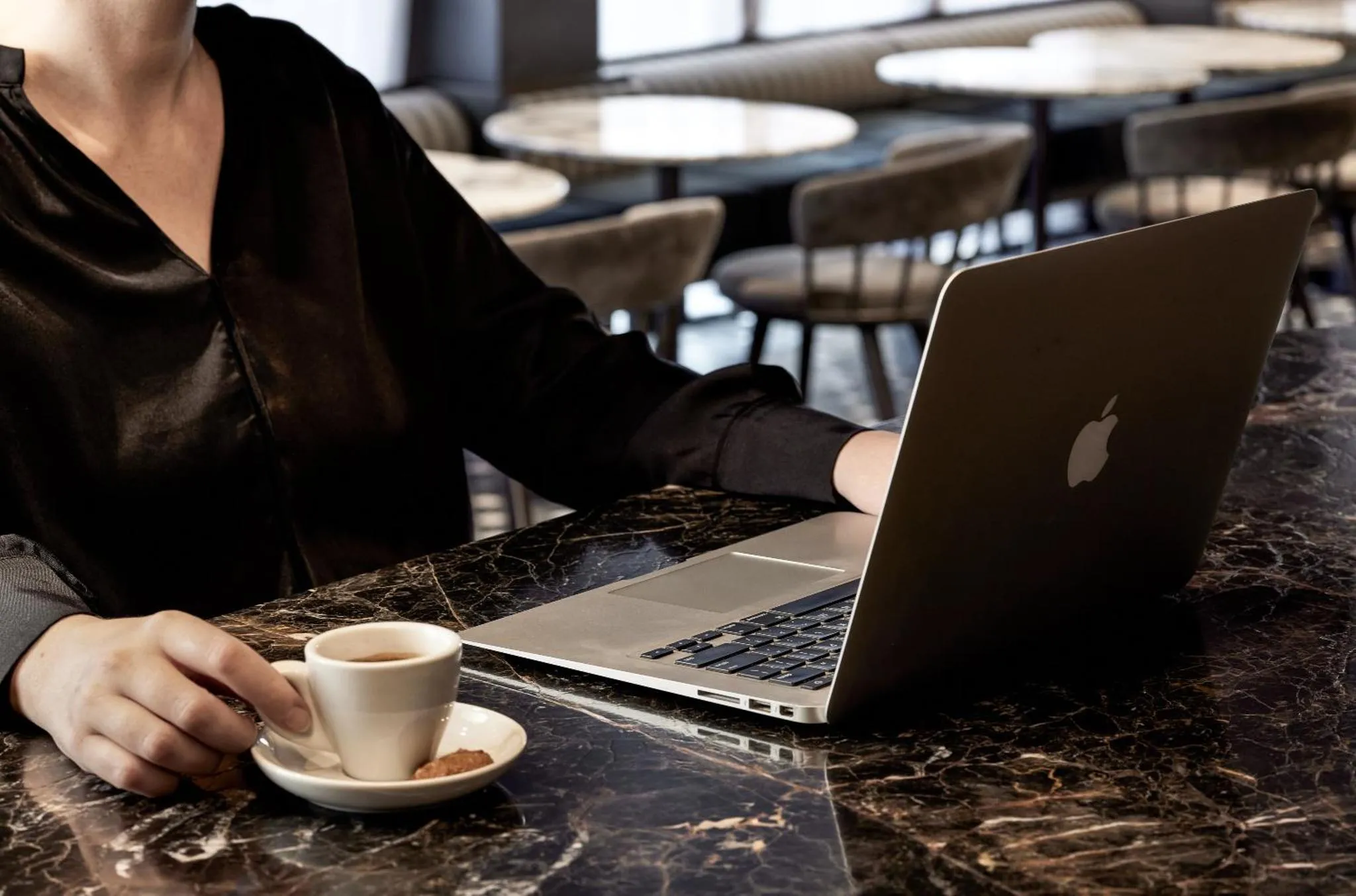 Une personne travaille sur un ordinateur portable devant une tasse de café sur une table en marbre.