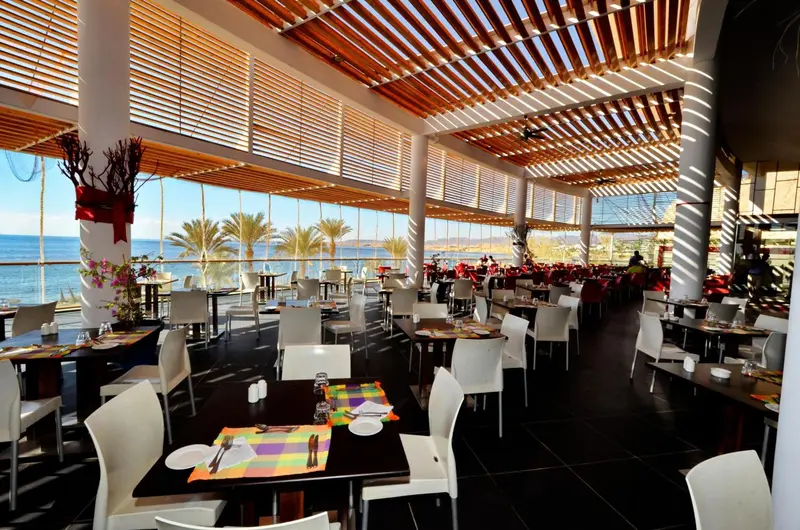 Une salle de restaurant lumineuse avec de grandes baies vitrées donnant sur la mer.