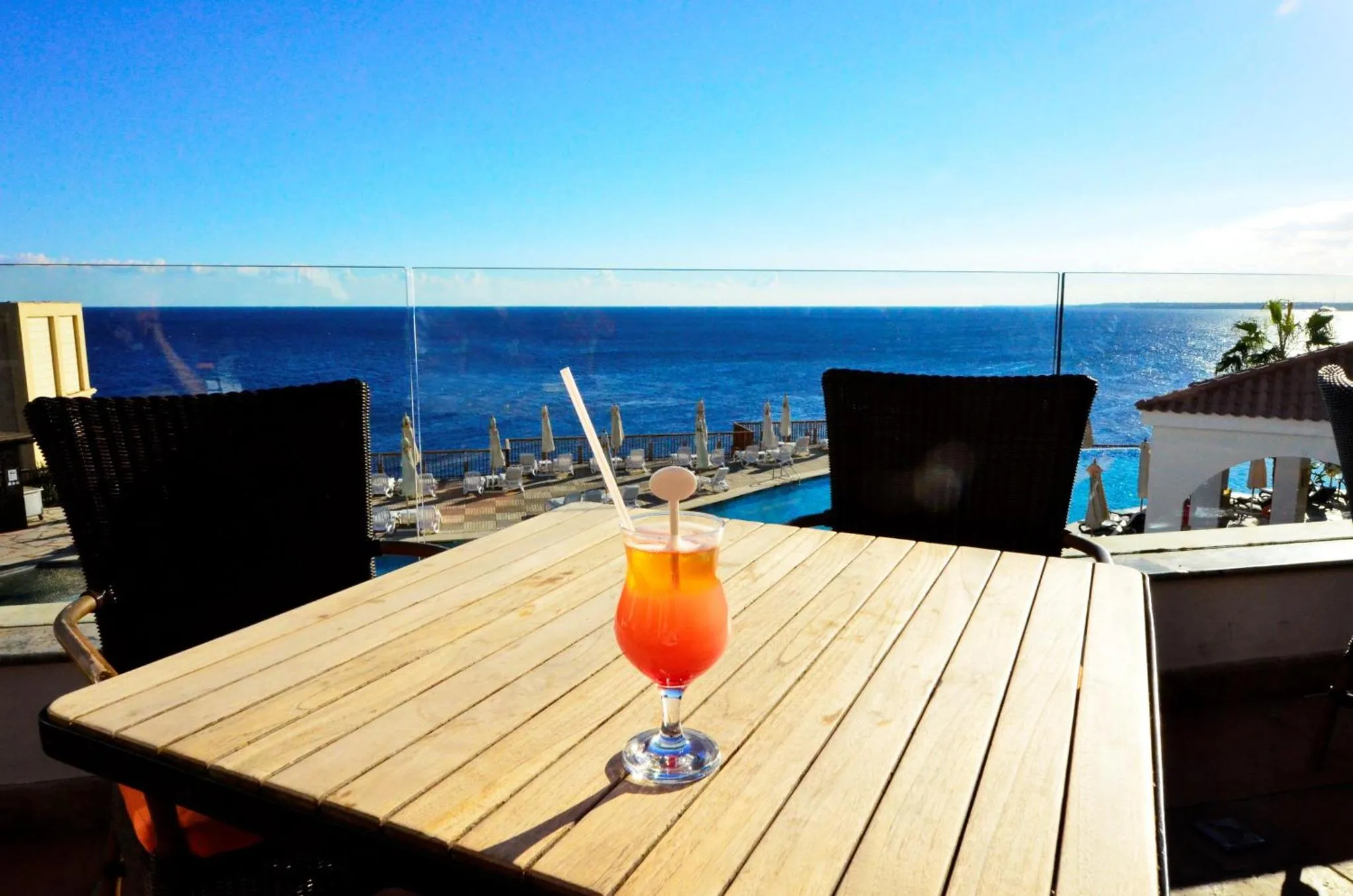 Une table en bois avec un cocktail coloré, face à la mer.
