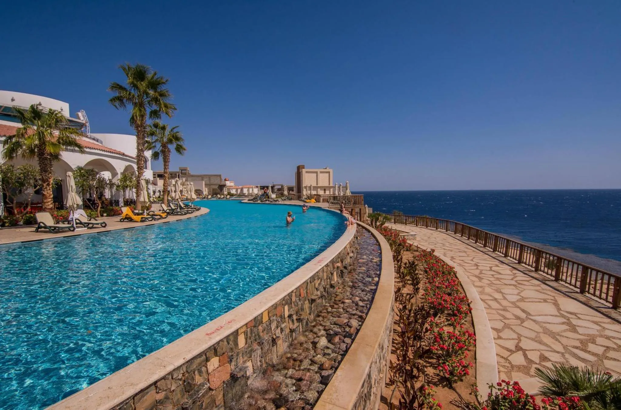 Une piscine sinueuse bordée d'une terrasse ensoleillée avec vue sur la mer.