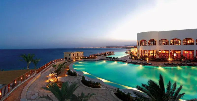 Vue d'une piscine d'hôtel au crépuscule avec la mer en arrière-plan.