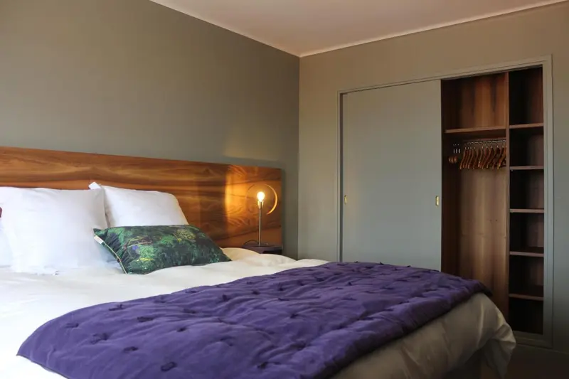 Une chambre avec un lit recouvert d'une couverture violette et un placard intégré.