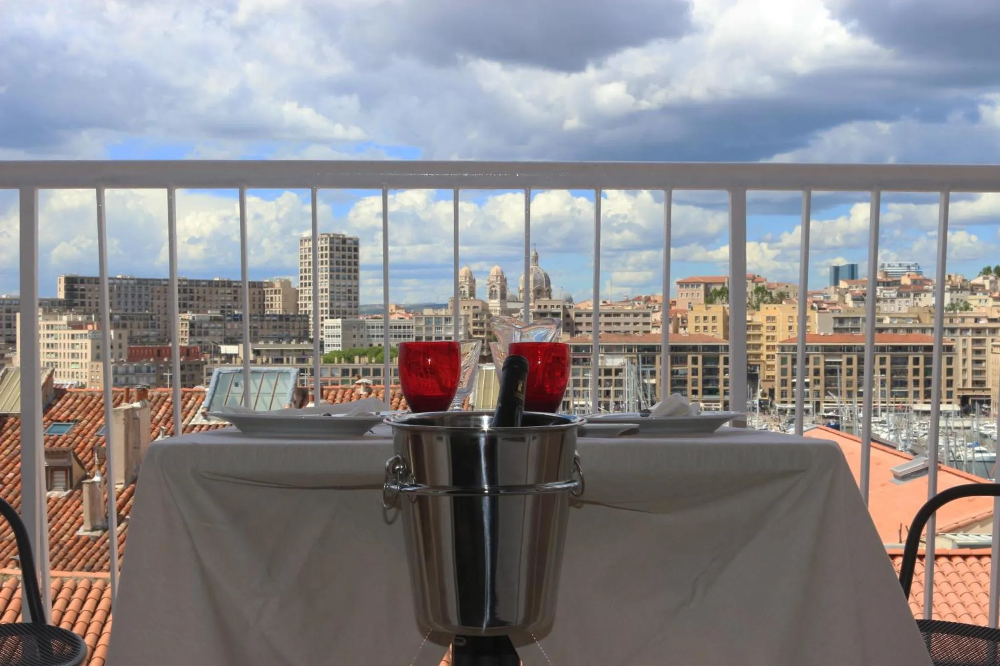 Table dressée avec deux verres de vin et une bouteille dans un seau à glace, sur une terrasse avec vue sur la ville.